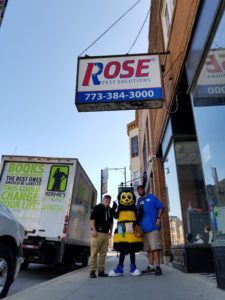 Rose Pest Book Donations Stand on a city sidewalk under a "Rose Pest Solutions" sign next to a truck