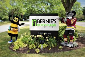 A person in a bee costume and another in a wolf costume stand on either side of a "Bernie's Book Bank" sign