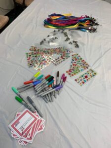Table set for Girl Scout Spark Day with colorful lanyards, stickers, Sharpie markers, and name tag cards neatly arranged on a white cloth.