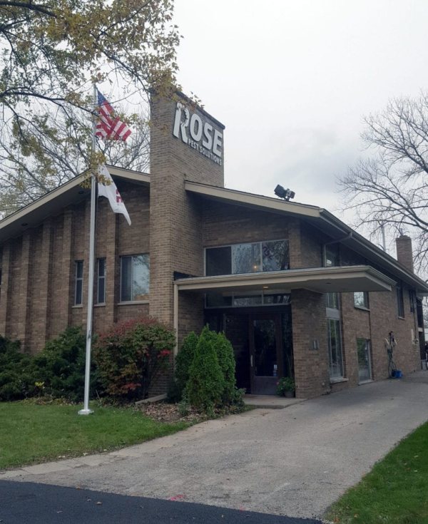 A brick building with a sign reading "Rose Pest Solutions," two flagpoles in front, and a driveway leading to the entrance on a cloudy day—your trusted choice for Northfield pest control.