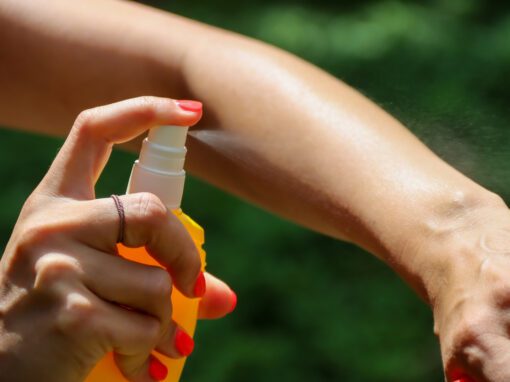 A person sprays liquid from a yellow bottle onto their forearm, following one of A Dozen Dos and Don’ts For Travel, with a blurred green background.