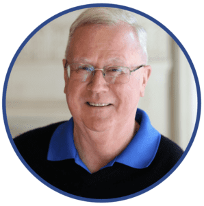 Dr. Stan Cope with short light hair, glasses, and a blue collared shirt under a dark sweater, smiling at the camera—ready to discuss trusted Mosquito Services for your home.