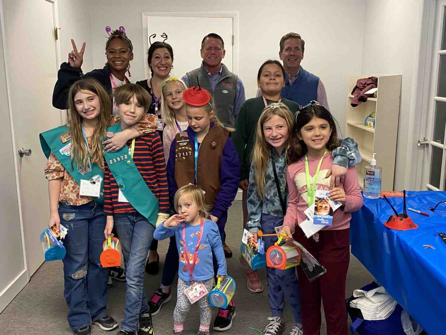 A group of children and adults posing with badges and crafts at an indoor event