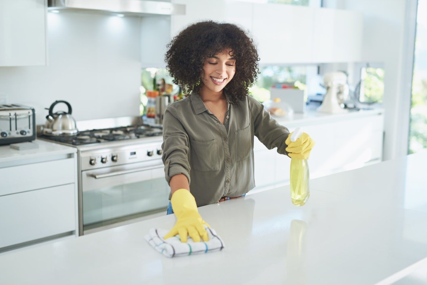 Person wearing gloves cleans a kitchen countertop with spray cleaner and cloth