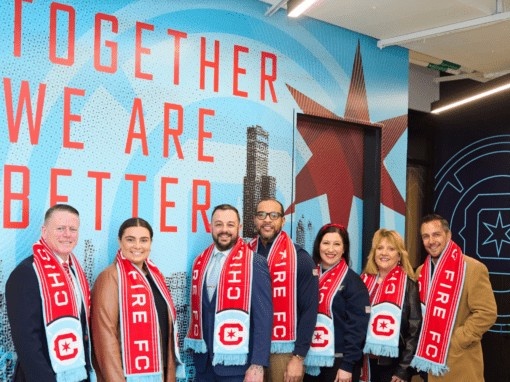 Six people wearing Chicago Fire FC scarves pose in front of a colorful wall mural
